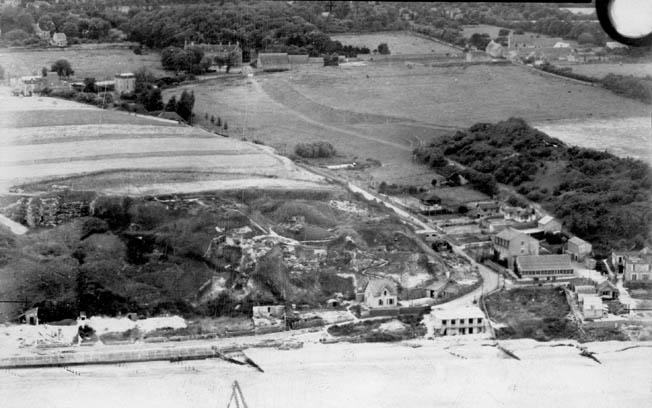 An aerial photograph taken by a Royal Air Force reconnaissance plane shows the Vierville Draw on June 30, 1943, almost a year before D-Day. The houses around the U-bend in the road were demolished by the Germans and replaced by strongpoints, pillboxes, and Widerstandsnests. 