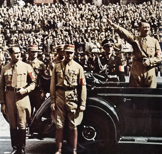 Deputy Führer Rudolf Hess (left) and brownshirt chief of staff Victor Lutze watch SS troops marching by as Adolf Hitler gives the Nazi salute from his Mercedes-Benz 770K, Nuremberg, 1938.