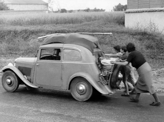 The former occupants of an automobile push the vehicle along a road somewhere in France after it has run out of gas. The roads from Paris into the French countryside were clogged with refugees fleeing the onrushing Germans, who invaded their country on May 10, 1940.