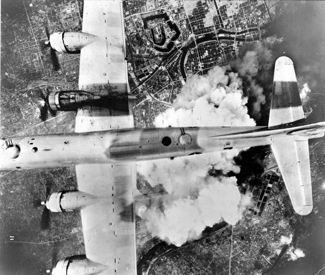 With smoke and dust rising below, a B-29 bomber flies over Osaka in June 1945.