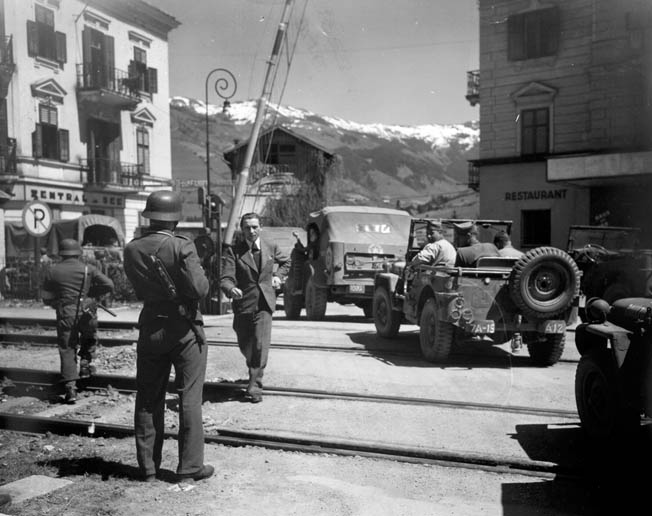 GIs in a convoy pass armed Germans providing security In Zell-am-See, Austria, just a few weeks after Germany surrendered.