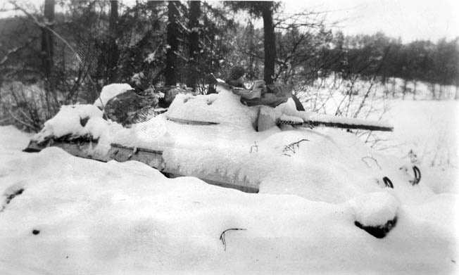 Joseph Pedraza, a T/5 with Troop B, 106th Cavalry Squadron, sits in the turret of a snow-blanketed armored car near Ludweiler, Germany, in January 1945. The armored car has been secreted in a trench dug by the cavalrymen of Troop B to provide better concealment. 