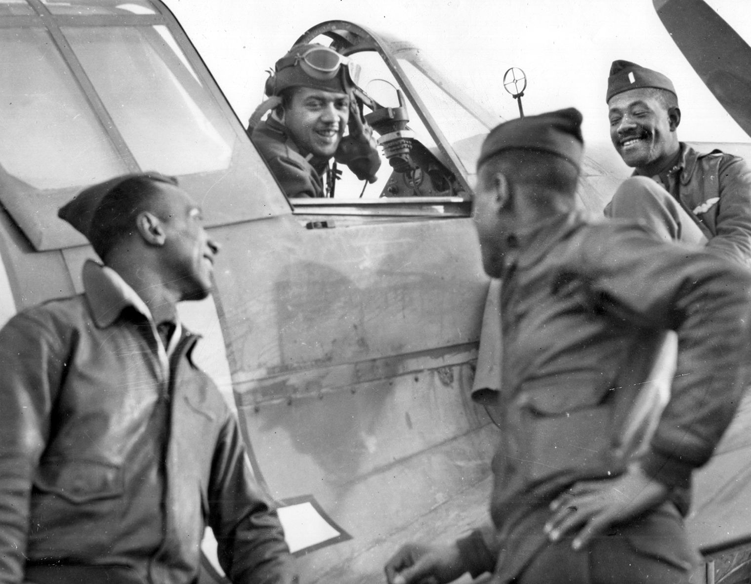 Though smiling for this photo, 99th Pursuit Squadron pilots Lieutenant W.V. Eagleson (in cockpit of his P-40) with Captain Lemuel R. Curtis, Lieutenant Charles B. Hall, and Lieutenant Willie Ashley and the rest of the Tuskegee Airmen were often frustsrated at being considered less capable then white pilots. 