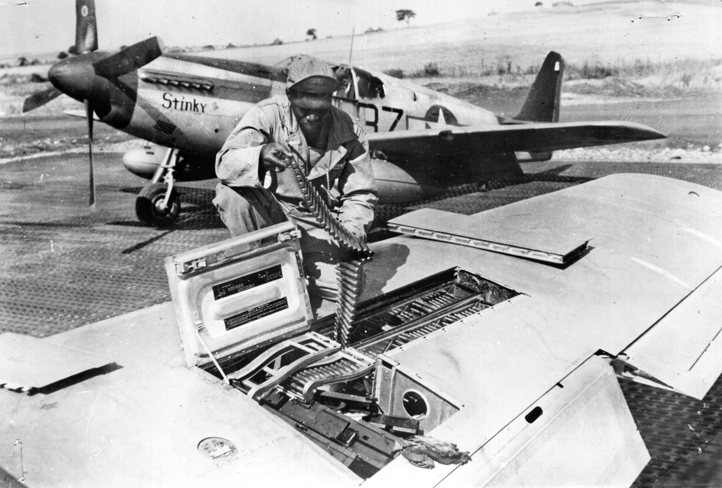 Private John Fields, an armorer with the 332nd Fighter Group, loads .50-caliber ammunition belts into the wings of a P-51 Mustang before a mission escorting 15th Air Force bombers over Germany.