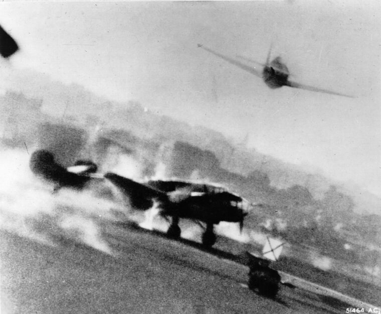 A P-47 Thunderbolt fighter catches an aircraft on the ground and sets it ablaze during a strafing run. The plane is probably a Potez 63, of French manufacture and in service of the Germans after its capture. 