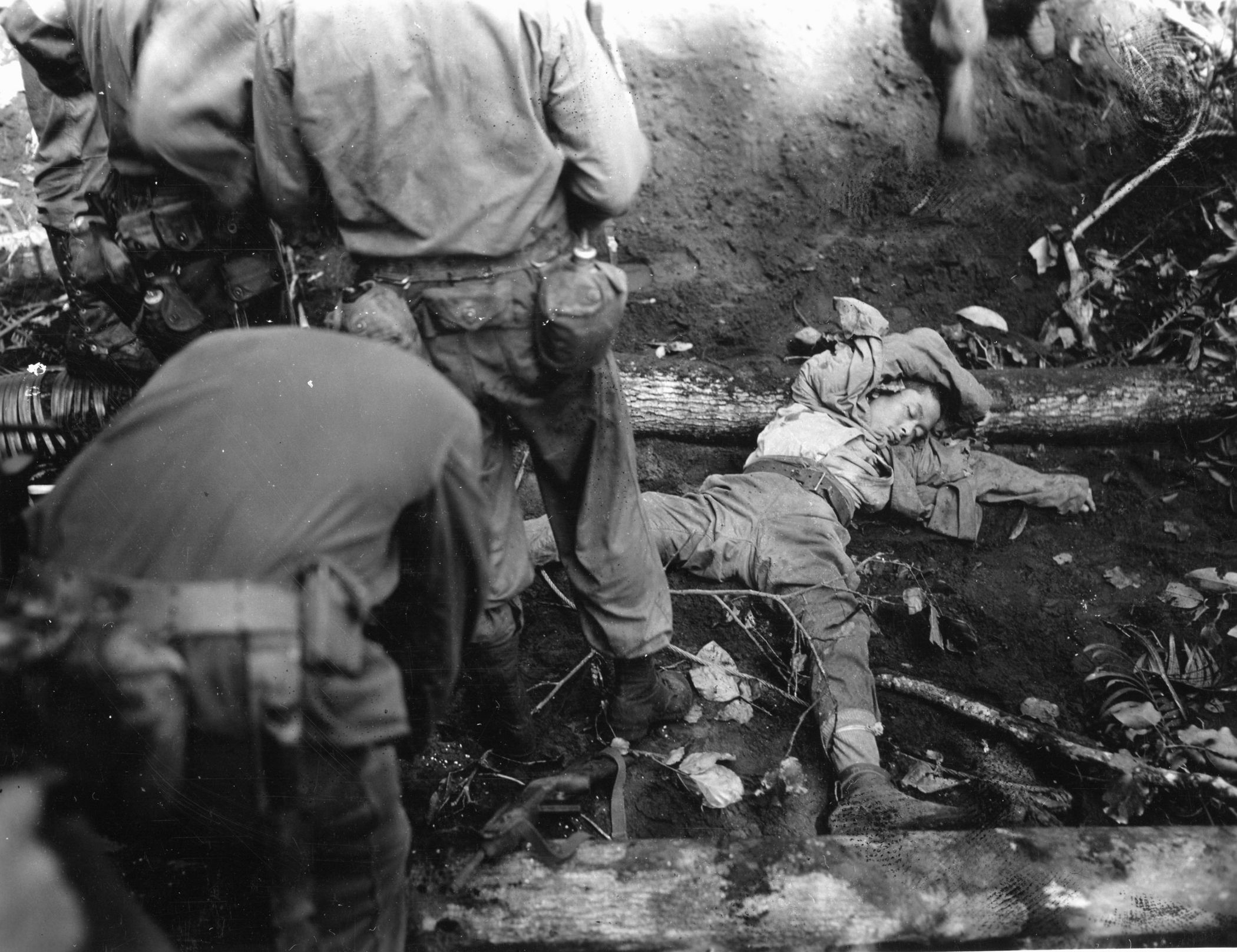 A dead Japanese soldier lies sprawled on the floor of the New Britain jungle.  Although he was killed in action, the soldier appears to have been starving. Reports of shortages of food and water among the Japanese defenders were widespread. 