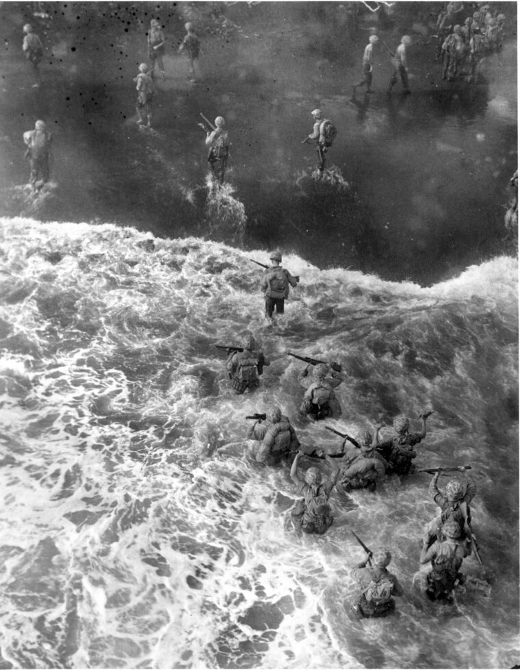 Laden with combat gear, U.S. Marines hold their M-1 rifles high above their heads and wade ashore in the pounding surf at Cape Gloucester on December 26, 1943. Days of difficult fighting lay ahead for the Americans.