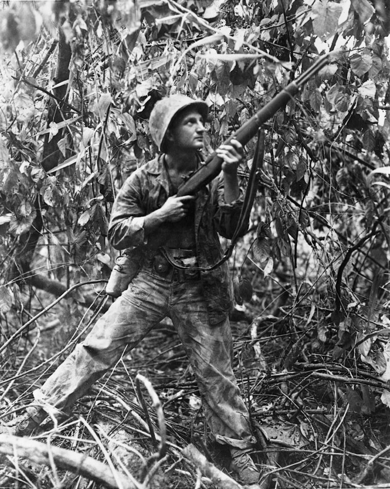 Looking upward, a Marine holds his rifle at the ready. Japanese soldiers, with .25-caliber Arisaka rifles, were known to have tied themselves high in the branches of trees to fire at American troops. 