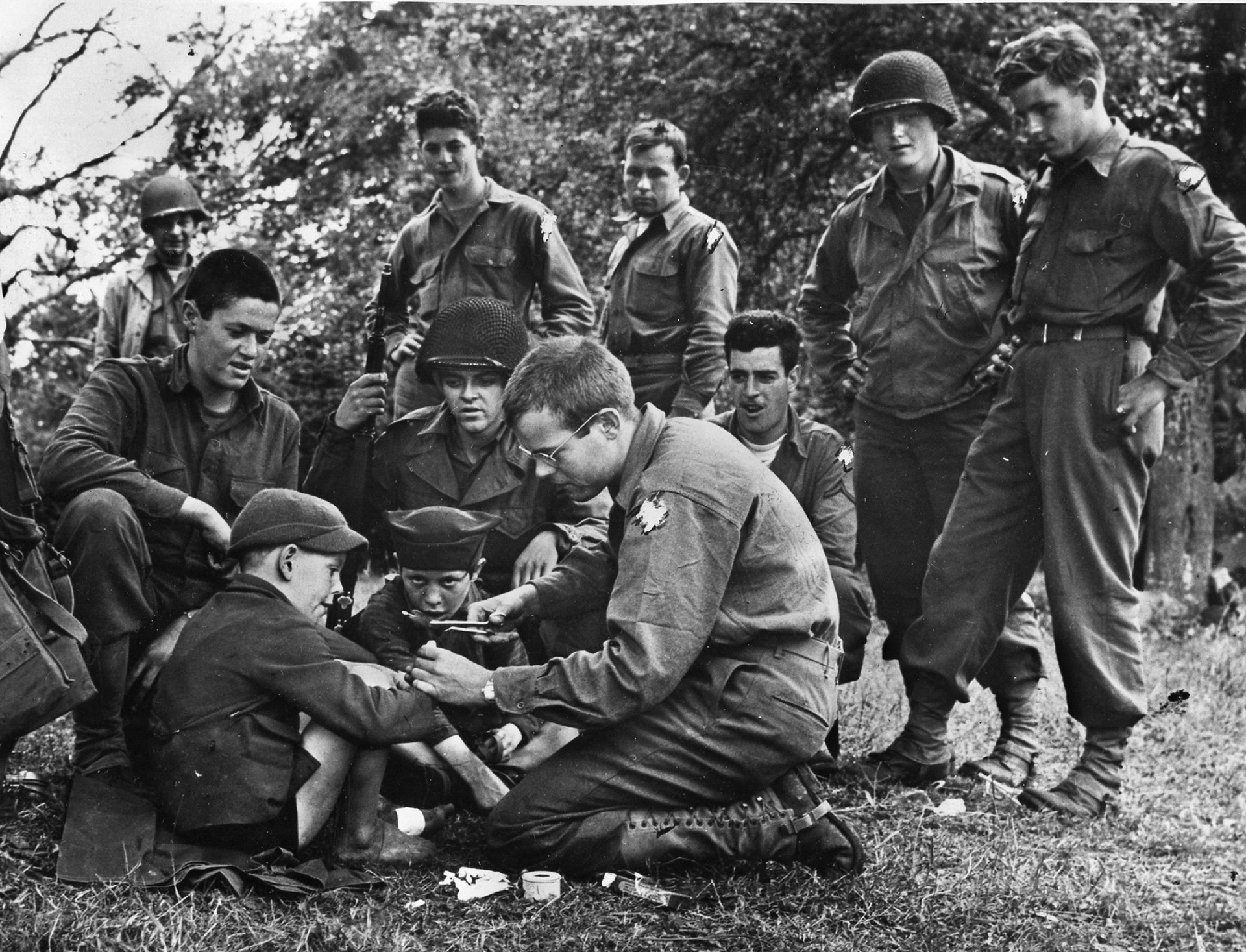 A private treats a small French boy’s hand while other soldiers watch. 