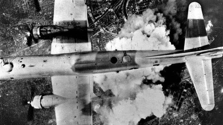 With smoke and dust rising below, a B-29 bomber flies over Osaka in June 1945.
