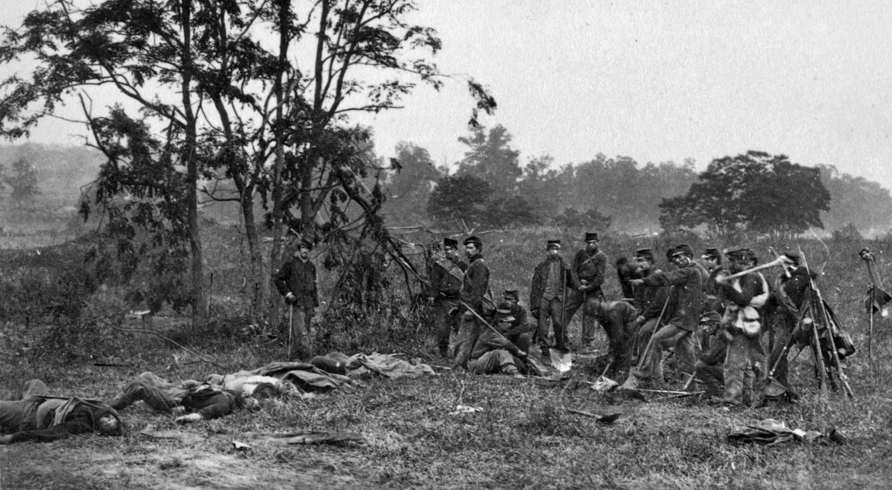 An exhausted Union burial detail takes a break from its melancholy work on the Miller Farm at Antietam. Dead Confederates awaiting interment lie scattered before them.