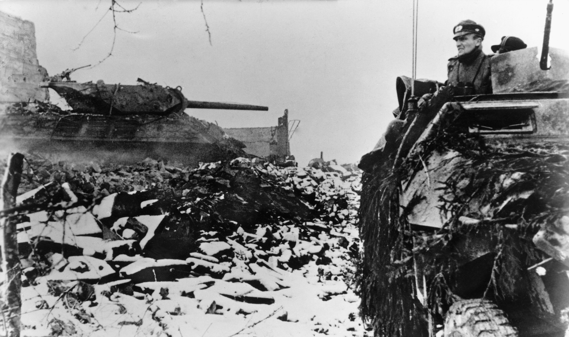 A German half-track advances past a disabled American tank destroyer on December 20, 1944, during Operation Wacht em Rhein.