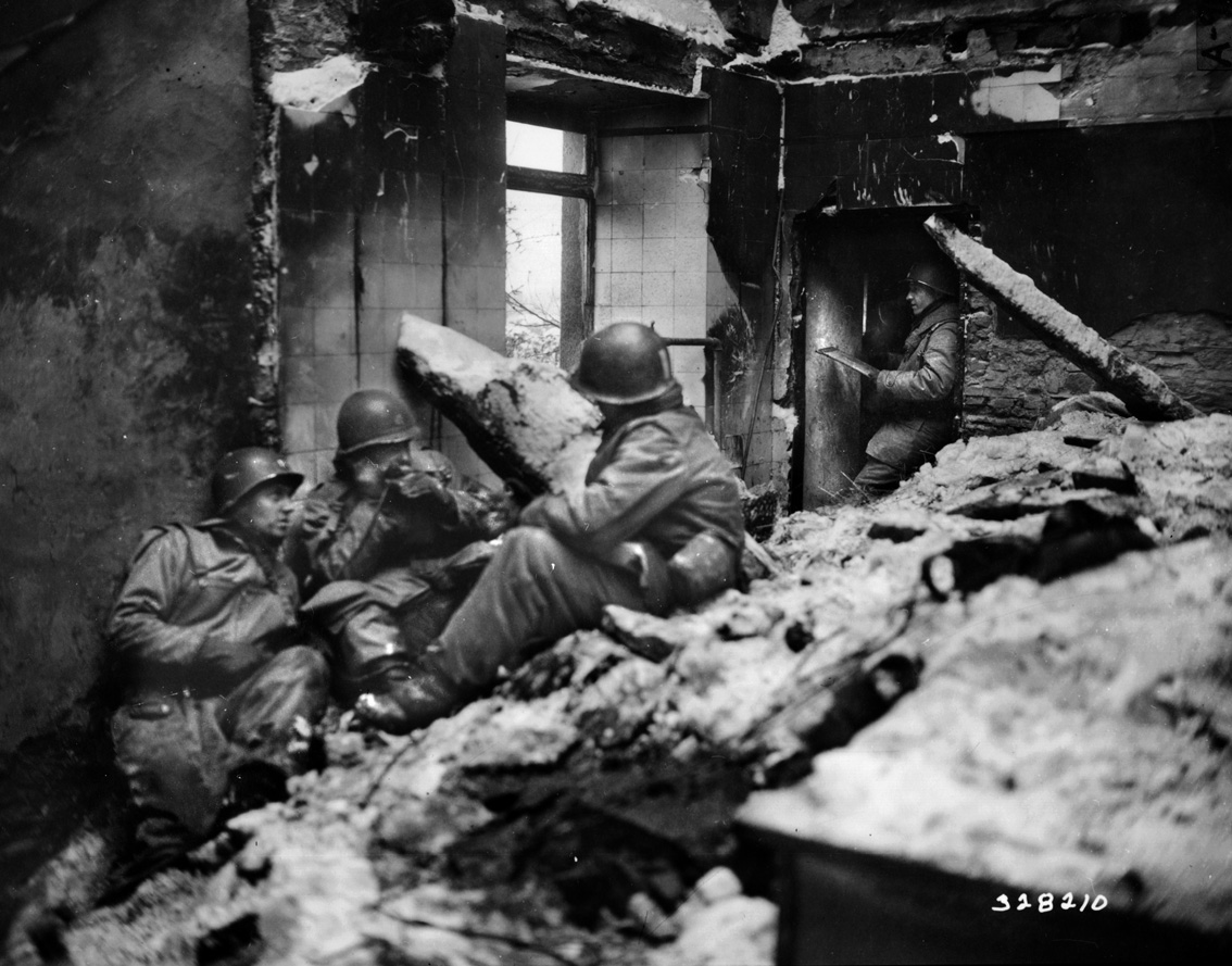American soldiers huddle amid the rubble of destroyed buildings 20 kilometers east of Bastogne in Wiltz, Luxembourg.