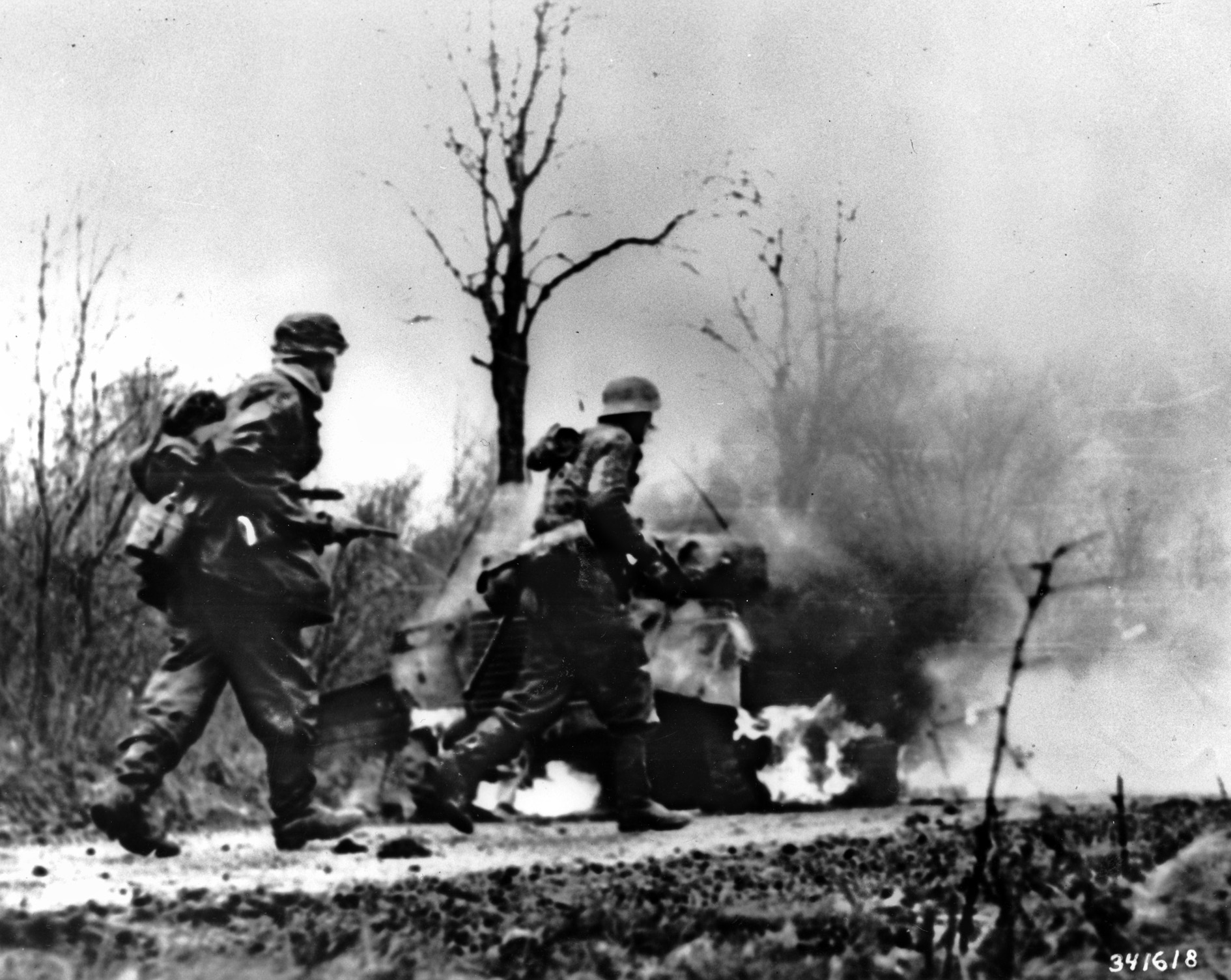 SS panzergrenadiers advance past burning American vehicles in German film footage that may have been staged for propaganda purposes.