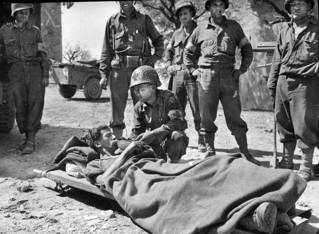 An American medic provides a drink of water to a wounded German prisoner somewhere in Italy. “Commando” Charles E. Kelly was a one-man destructive force in combat against the Germans, and this soldier may have been one of the casualties he inflicted on the enemy.