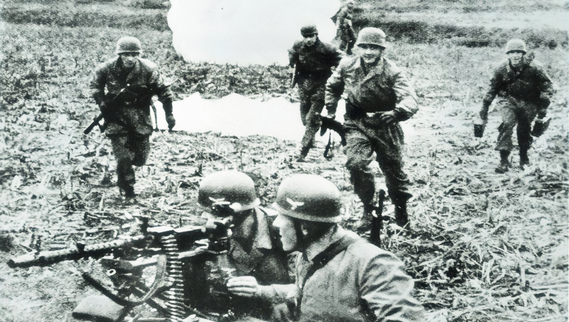 German paratroopers rally after landing as their comrades keep a watchful eye behind a menacing MG34 machine gun.