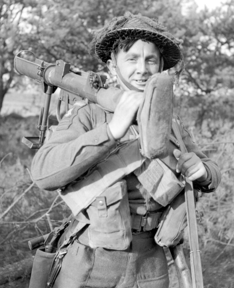A soldier of the Cornwall Regiment shoulders his PIAT as he moves toward the front.