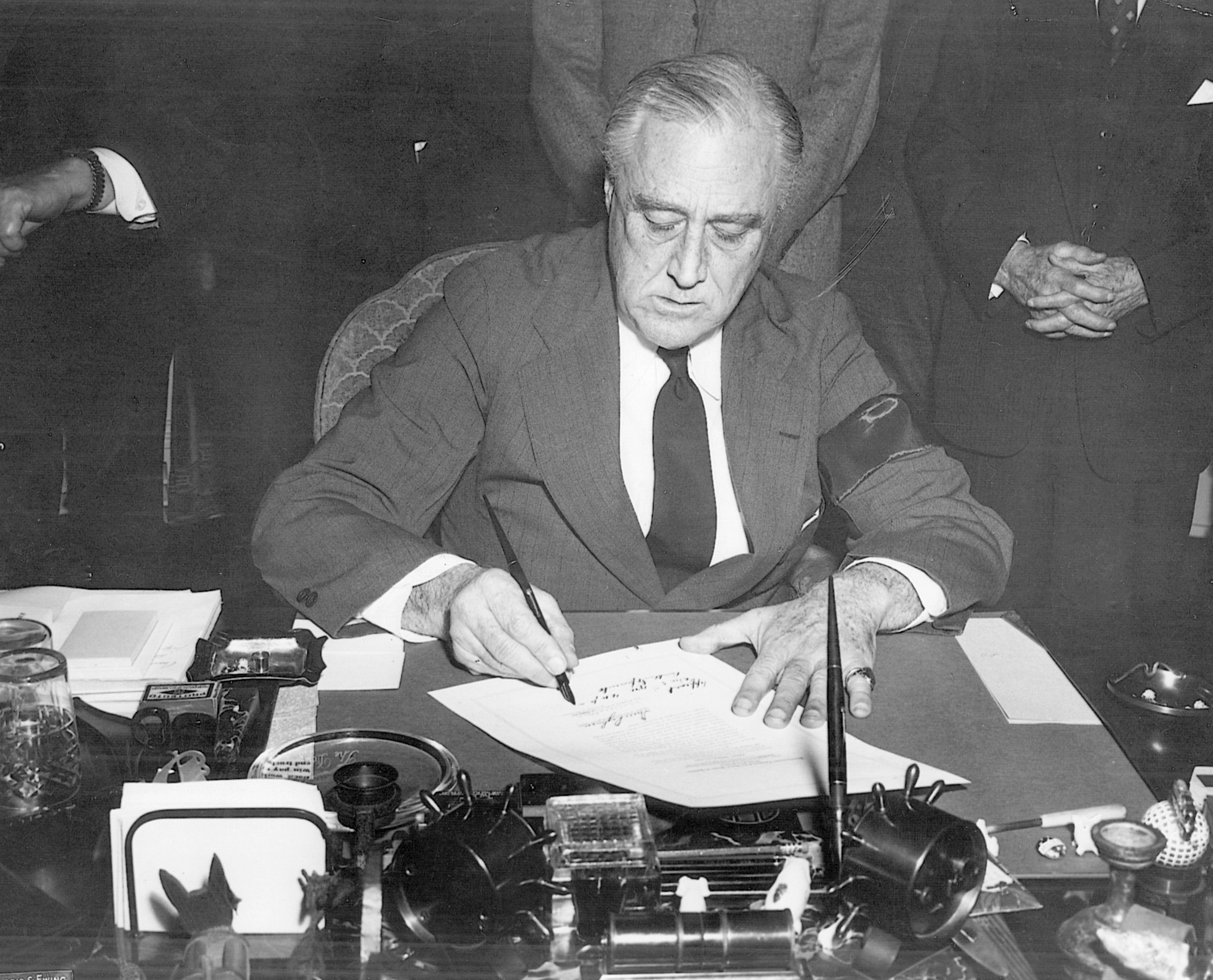 President Roosevelt, wearing a black mourning band, signs the declaration of war against Japan.