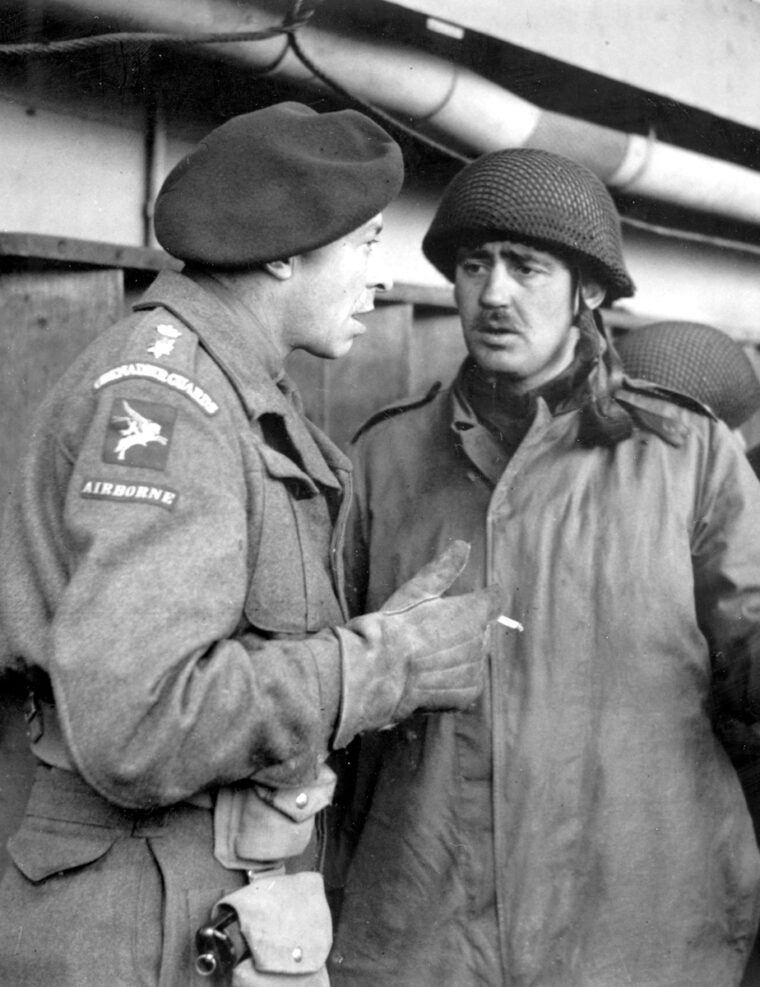 Major John Dutton Frost (right), leader of the commandos at Bruneval, discusses the raid with an Airborne officer. Here he examines a trophy of the raid surrounded by the commandos he dropped in France. 