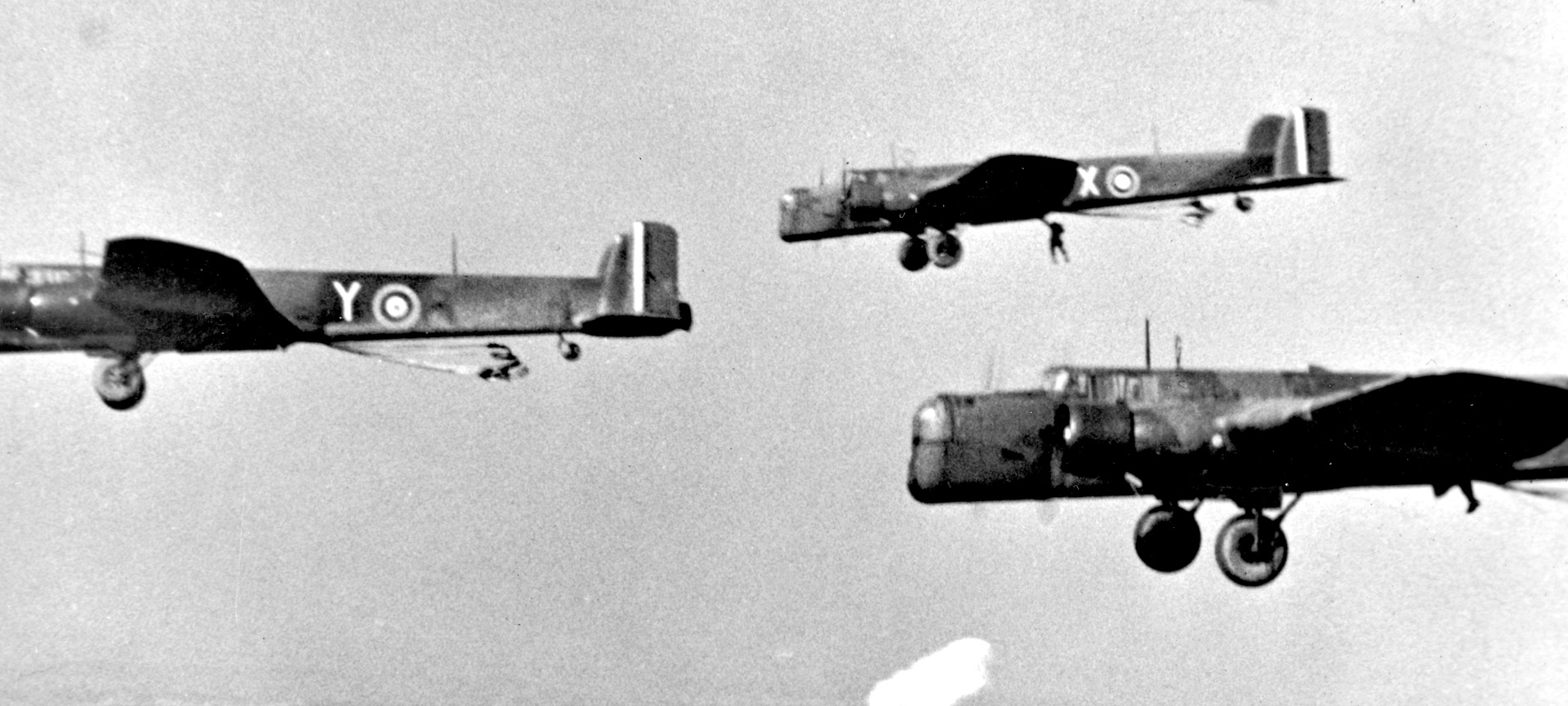 Royal Air Force Whitleys fly across the Bruneval drop zone. A commando is seen leaving the plane in the distance.