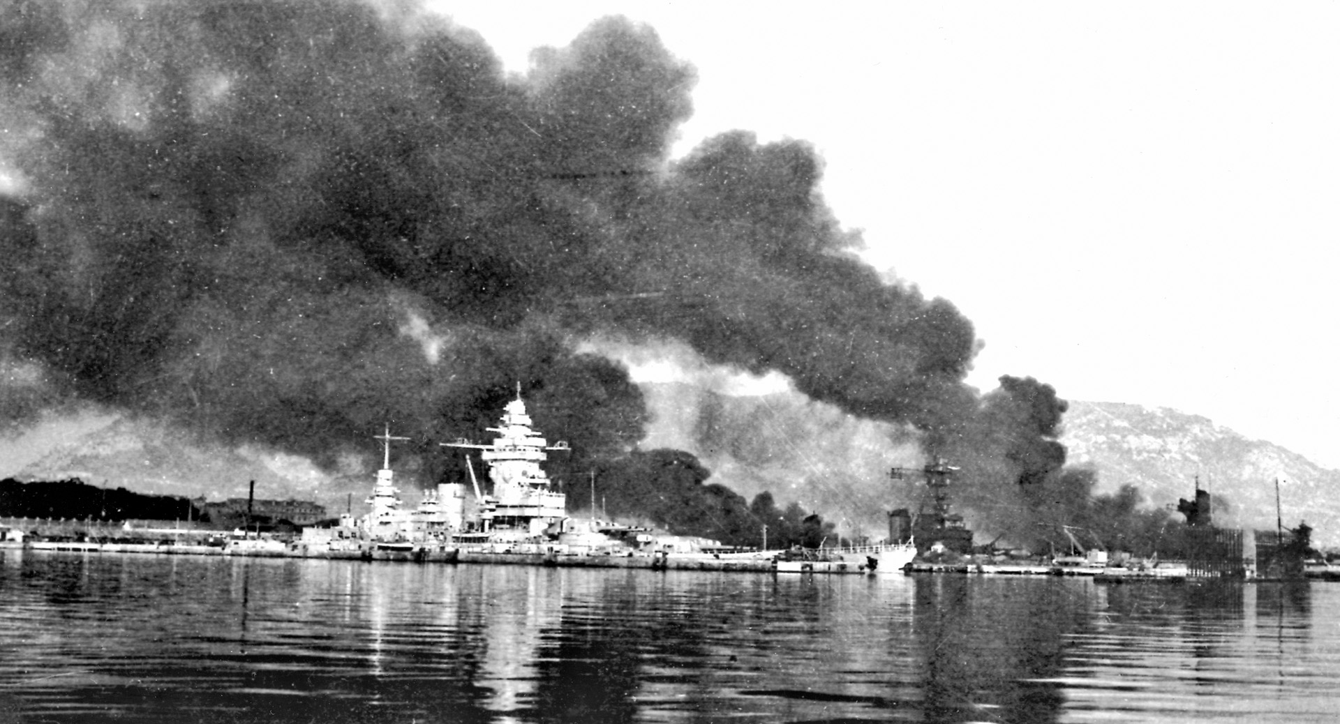 The French vessels Strasbourg, Colbert, and Algerie are seen against a backdrop of smoke and flames at Toulon. French sailors scuttled their own ships on November 27, 1942, to prevent their falling into German hands.