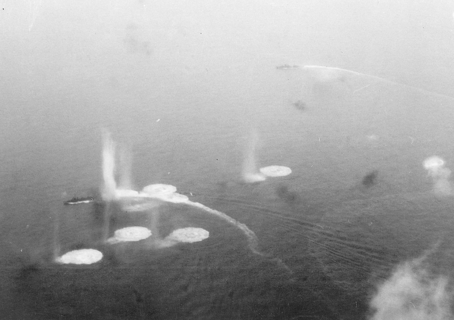 A Japanese destroyer maneuvers violently as American planes unleash their bombs. Another Japanese warship is visible in the distance.