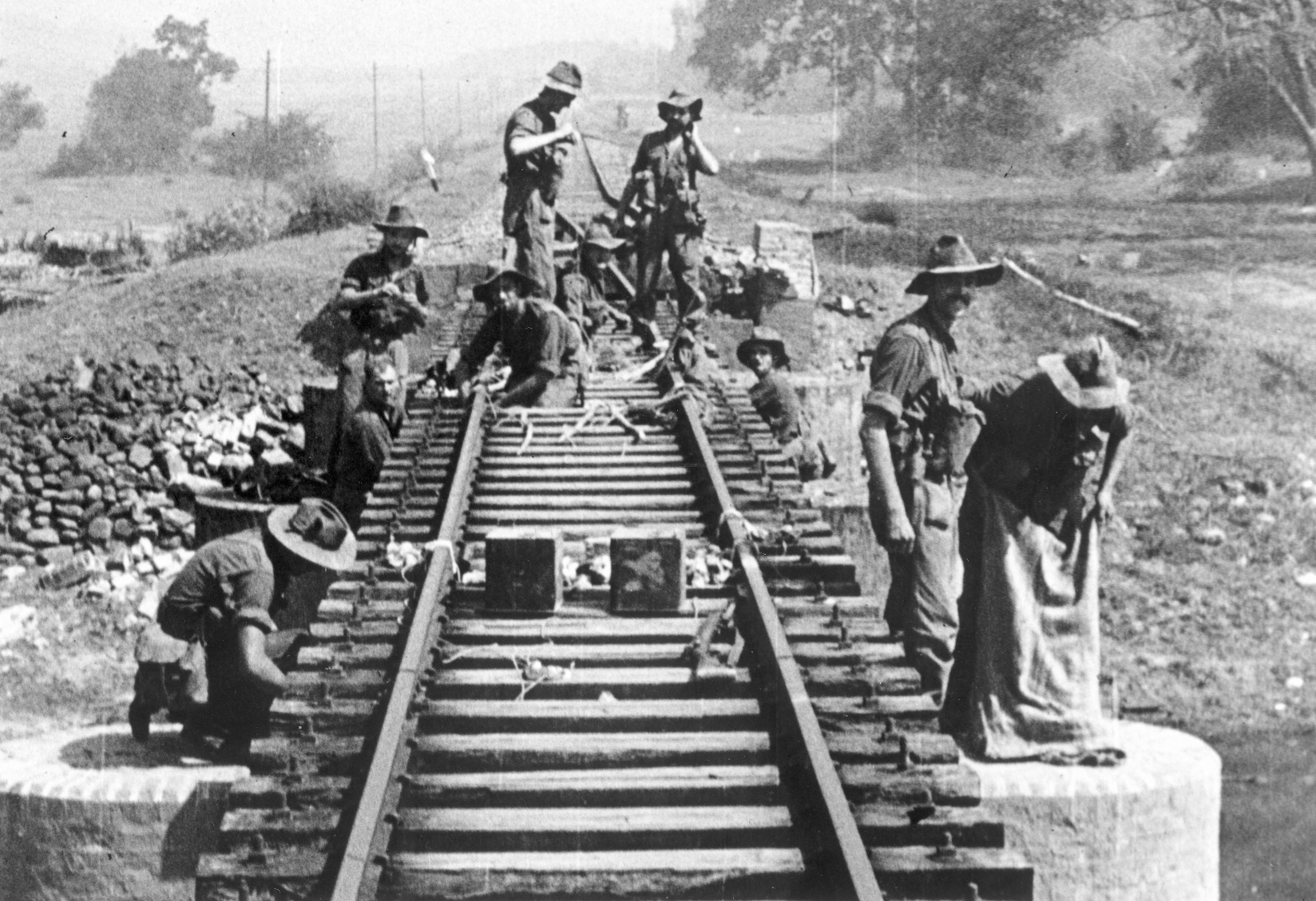 Wiring explosive charges, Chindits prepare a railroad bridge for demolition.