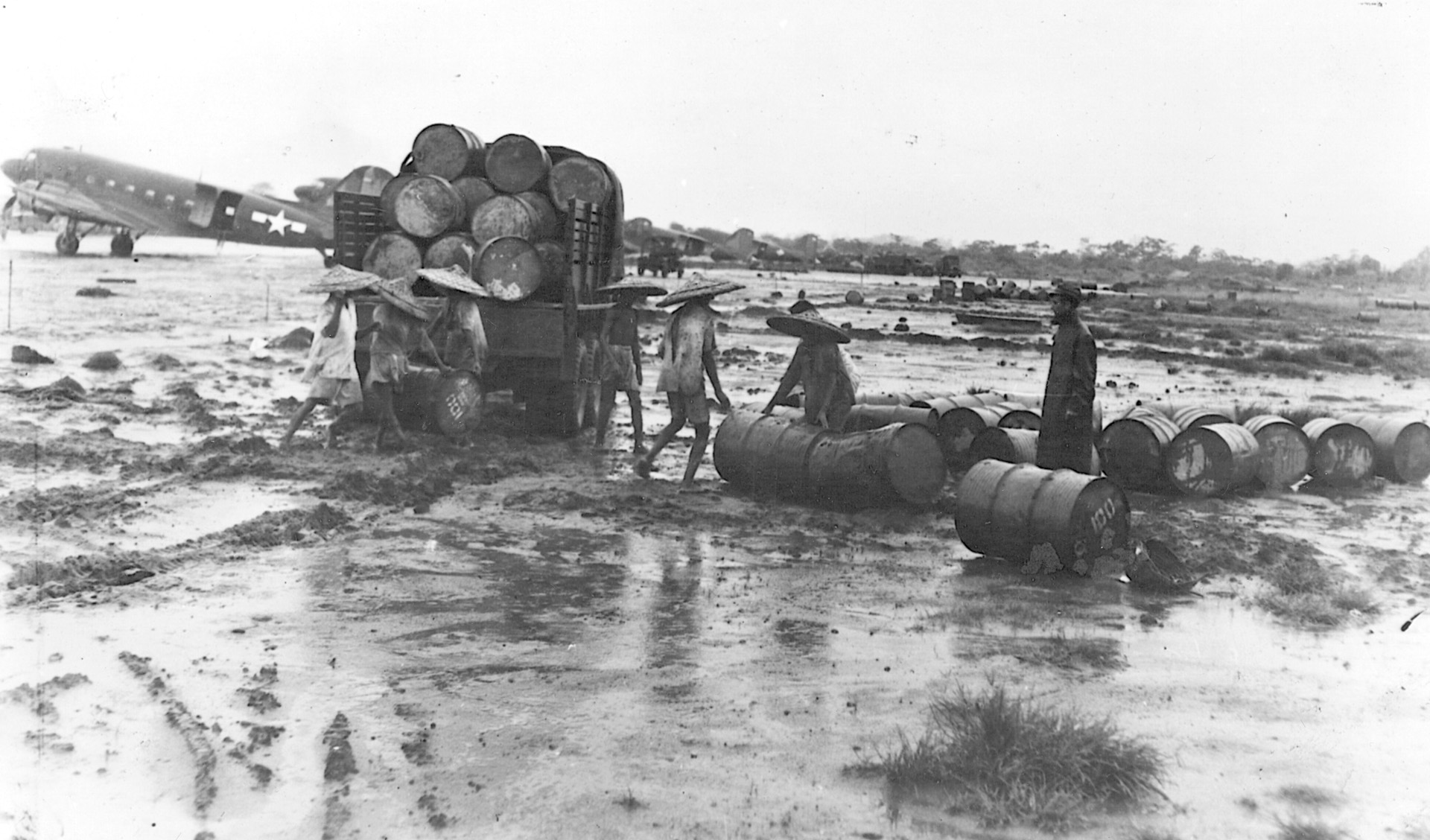 Laborers load empty gasoline drums at an air base in Assam, India, during the monsoon season.