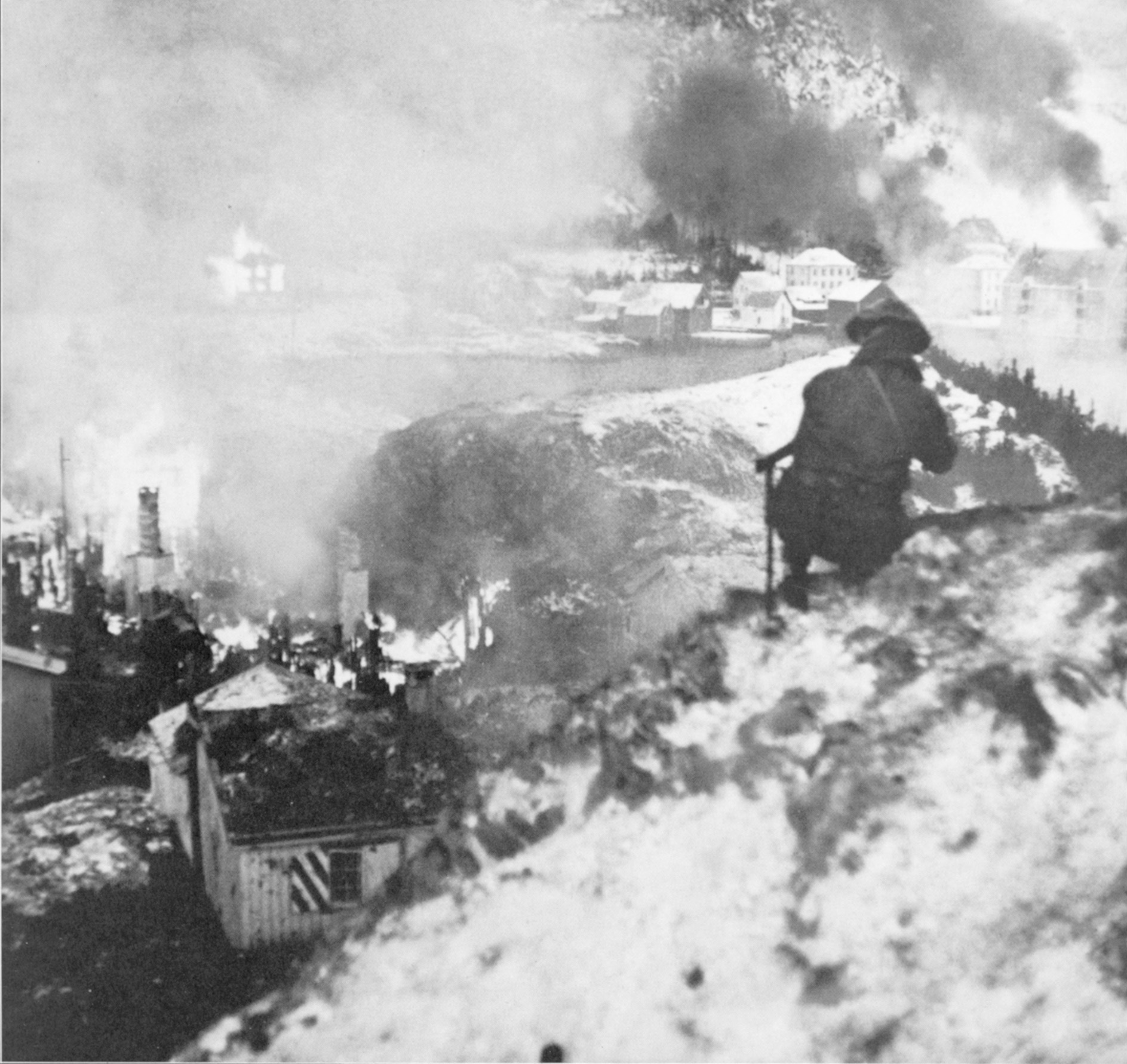 A British Commando on a hill above the demolished German barracks on Maaloy watches the action across the fjord in South Vaagso.