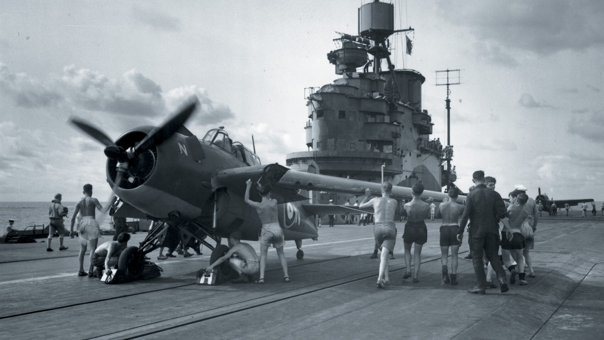 On the armored flight deck of the HMS Formidable crewmen fold the wings of a fighter plane that has just landed.