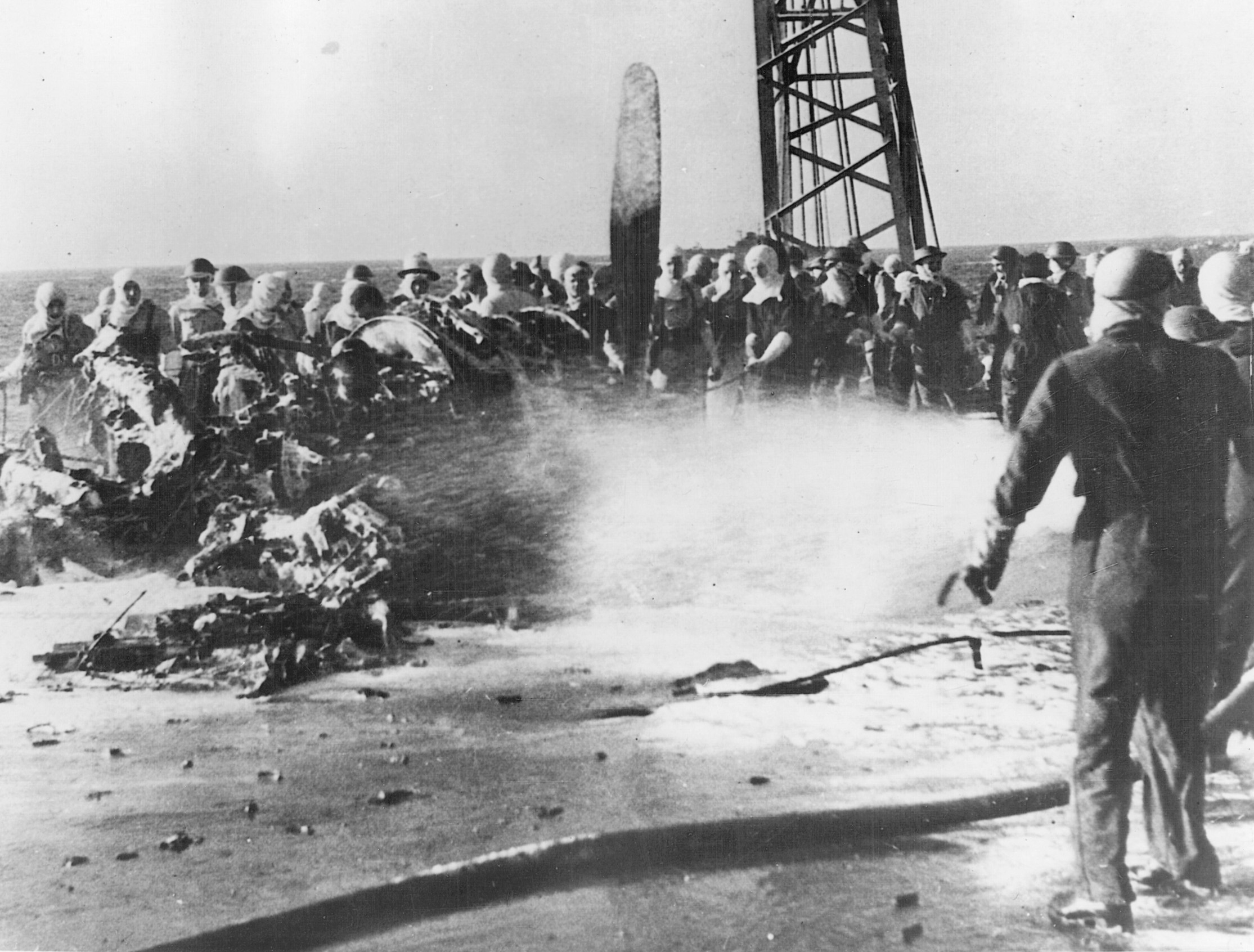 Fireman spray the wreckage of a Japanese kamikaze that has crashed into the armored flight deck of a British aircraft carrier.