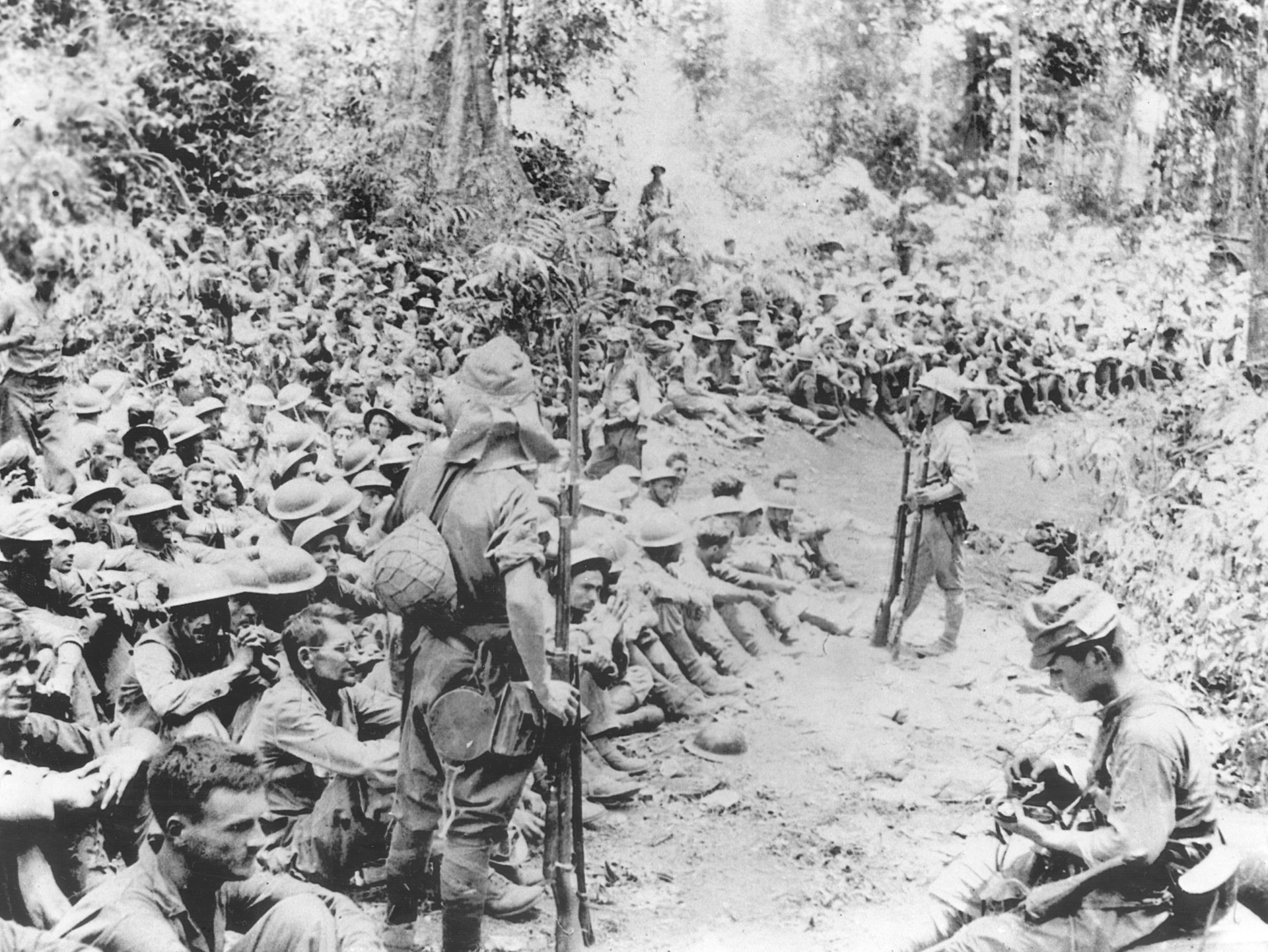 Under heavy Japanese guard, American captives sit along a dusty Philippine path and await instructions from their captors.
