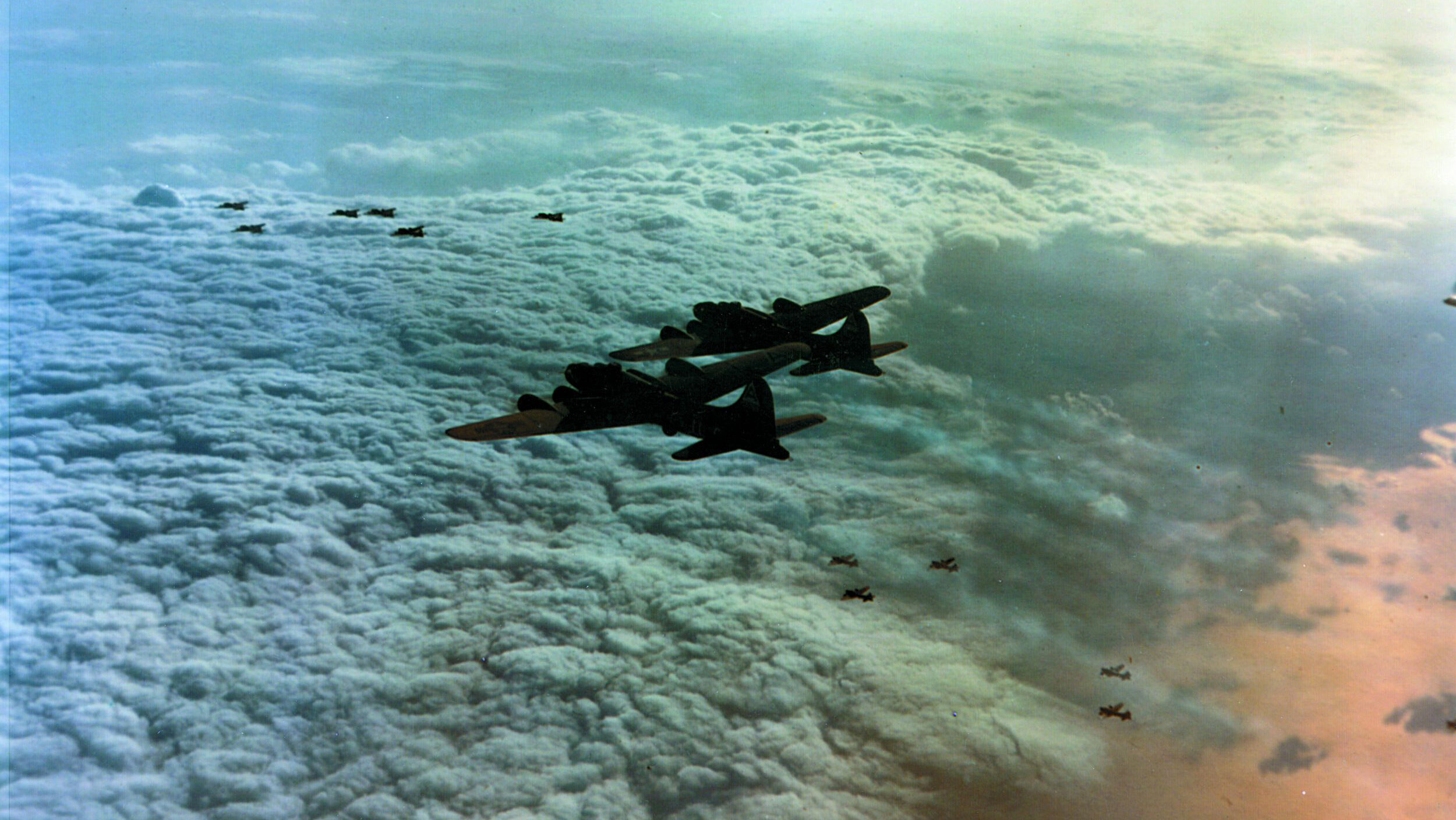 Flying high above sun-tinged clouds, a formation of Boeing B-17 Flying Fortresses streaks away from a target in Germany after dropping its cargo of destruction. The U.S. Eighth Air Force bombed German cities by day, while the British Royal Air Force kept up the round-the-clock air offensive at night.