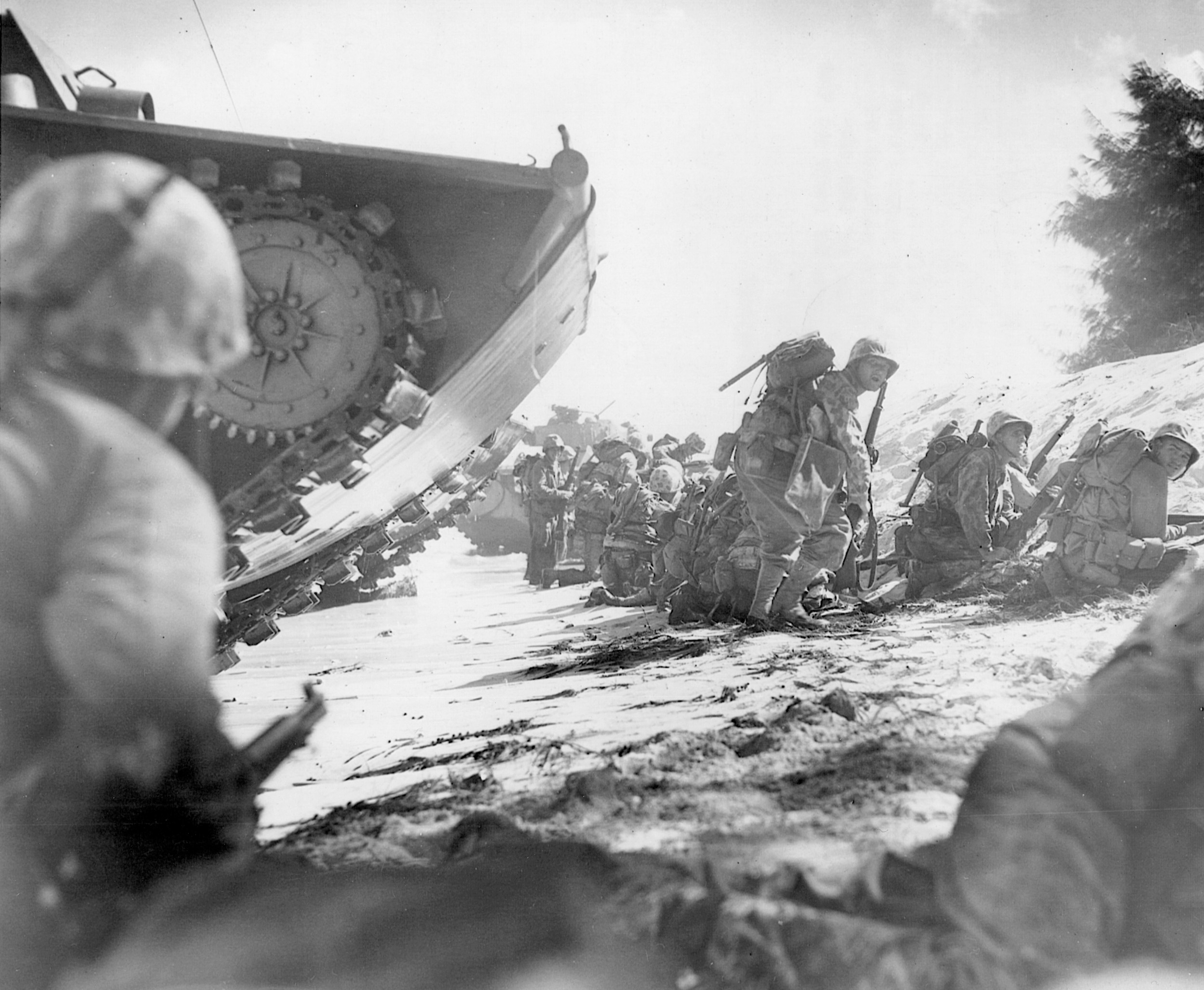 Marines of the first assault wave head inland on Saipan beyond the brow of a tracked vehicle called a Buffalo.