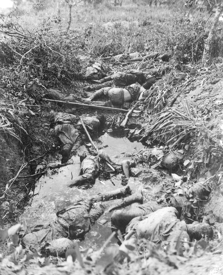 The bodies of Japanese soldiers killed in action lie half buried in a muddy Saipan shell hole.