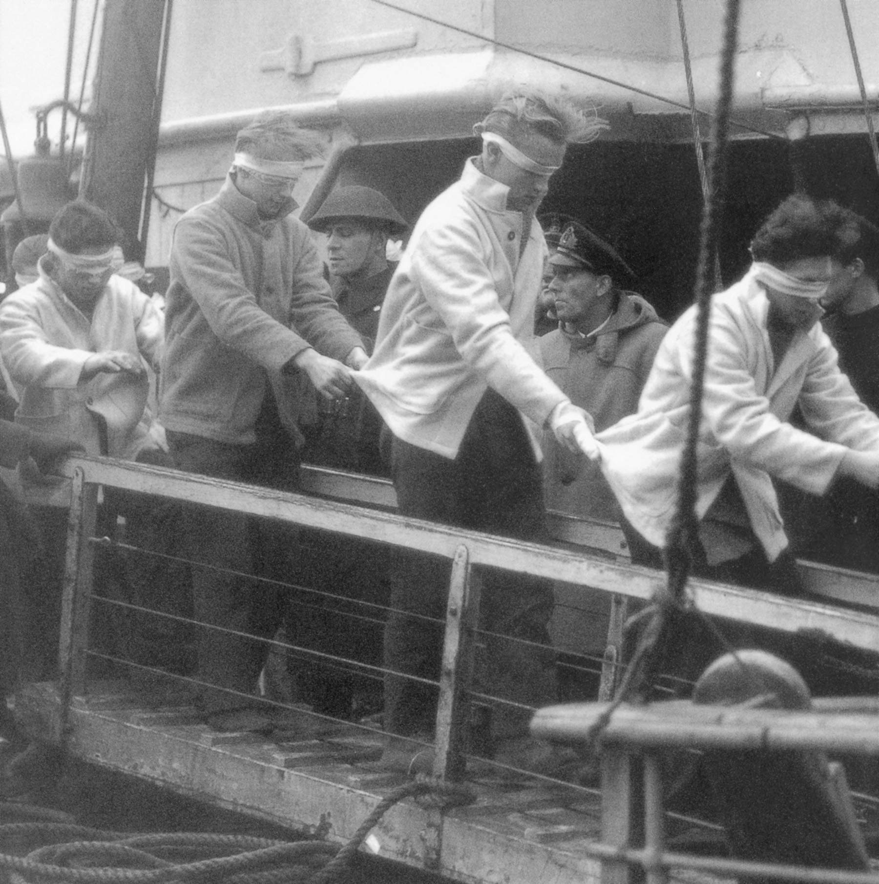 Blindfolded, a few of the 36 survivors of the sinking of the Scharnhorst are led down a gangway into captivity. The German battlecruiser had a complement of 2,000 men.