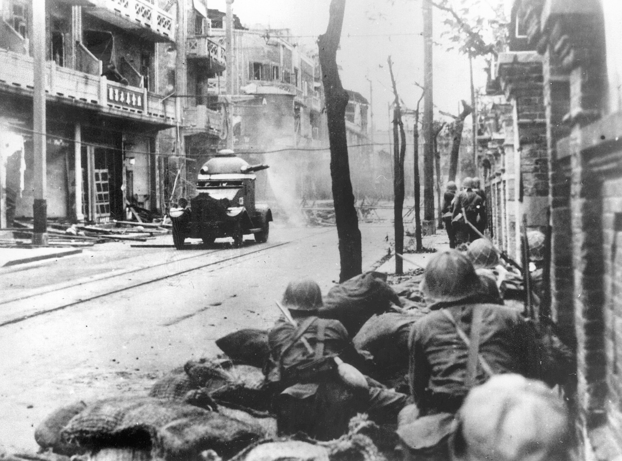  A French-built armored car is passed by a squad of advancing Japanese troops as they move warily along a shattered street in Shanghai.