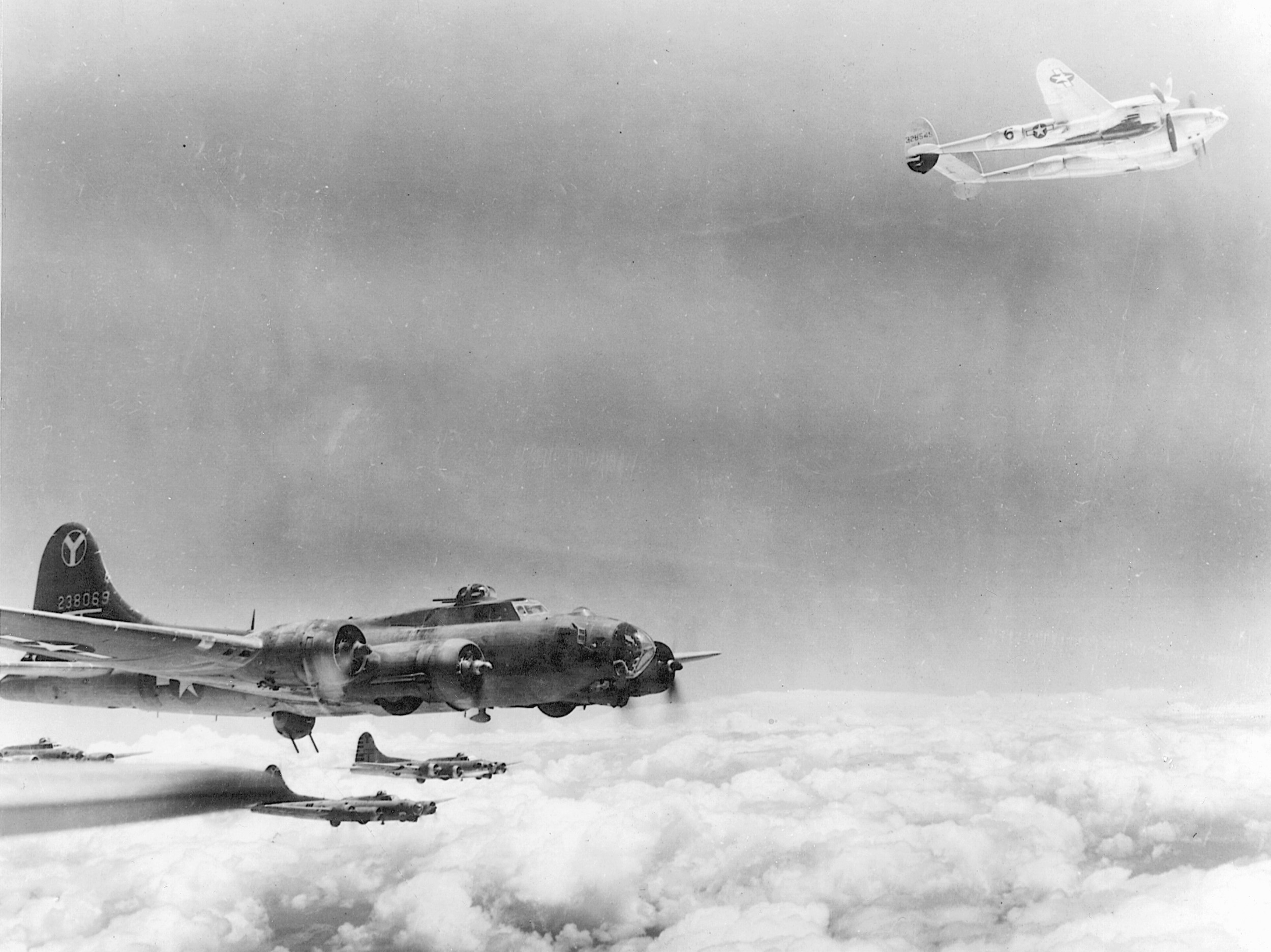 A P-38 escorts B-17 Flying Fortresses, July 1944. One of its propellers is feathered.