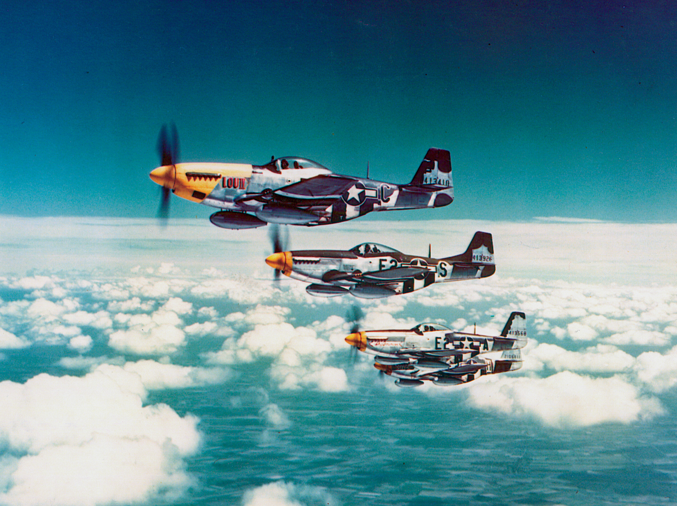 A group of P-51s falls into formation, drop tanks under the wings. 