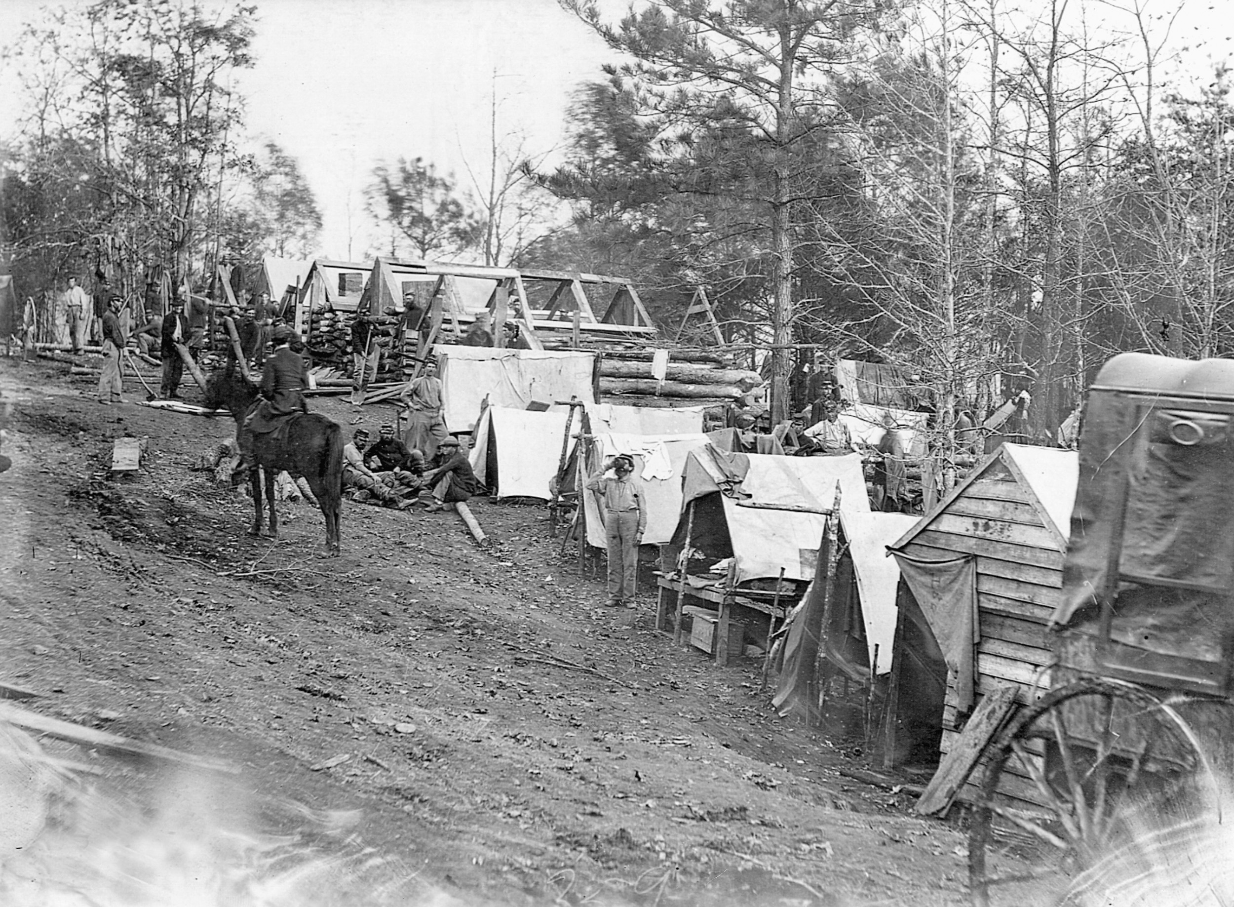 Soldiers construct log huts from nearby trees. One soldier takes a drink (center) while others split timbers (left) as a mounted officer looks on.