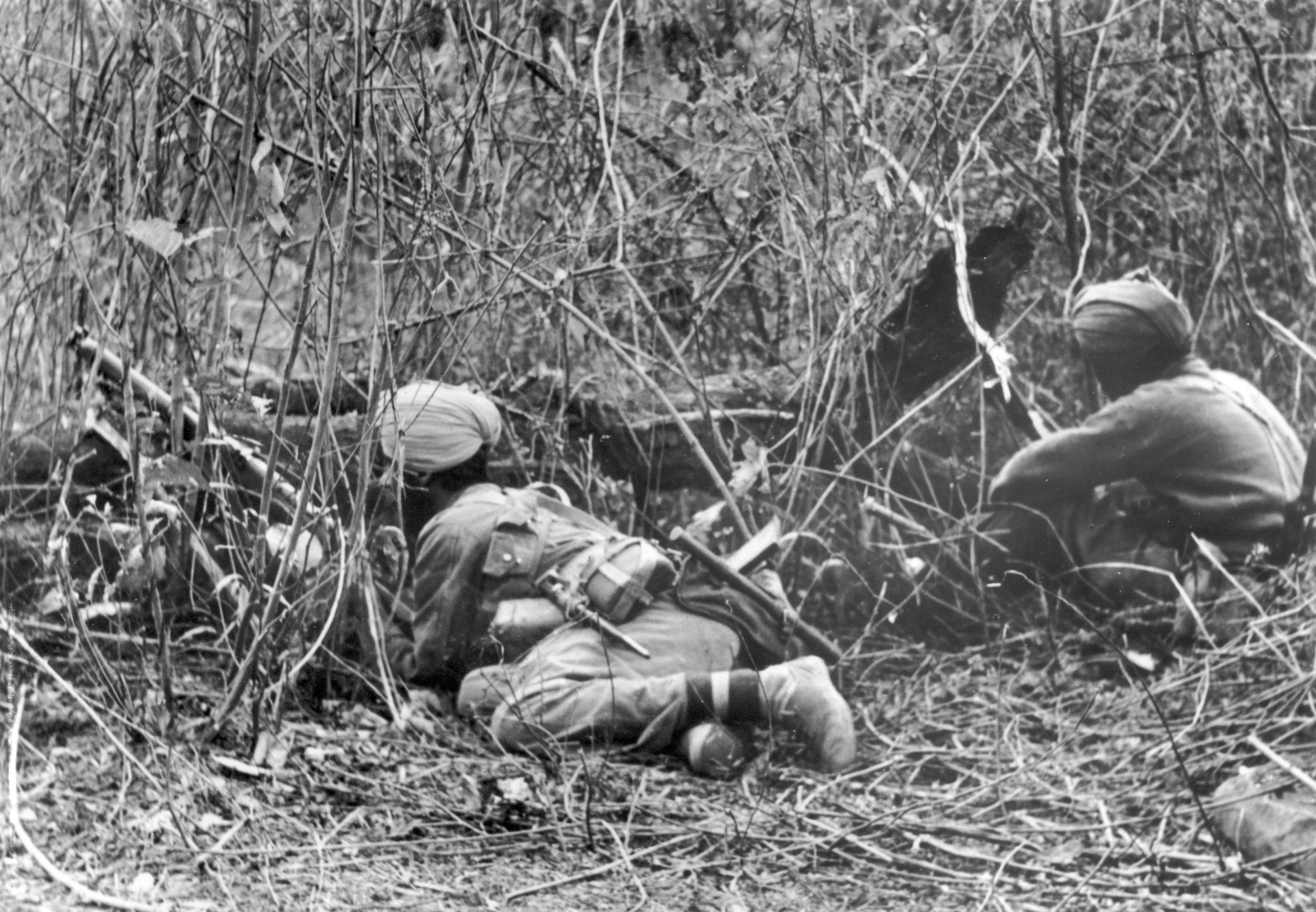 Two Sikhs, one with his rifle out in front of him, watch for Japanese infiltrators.