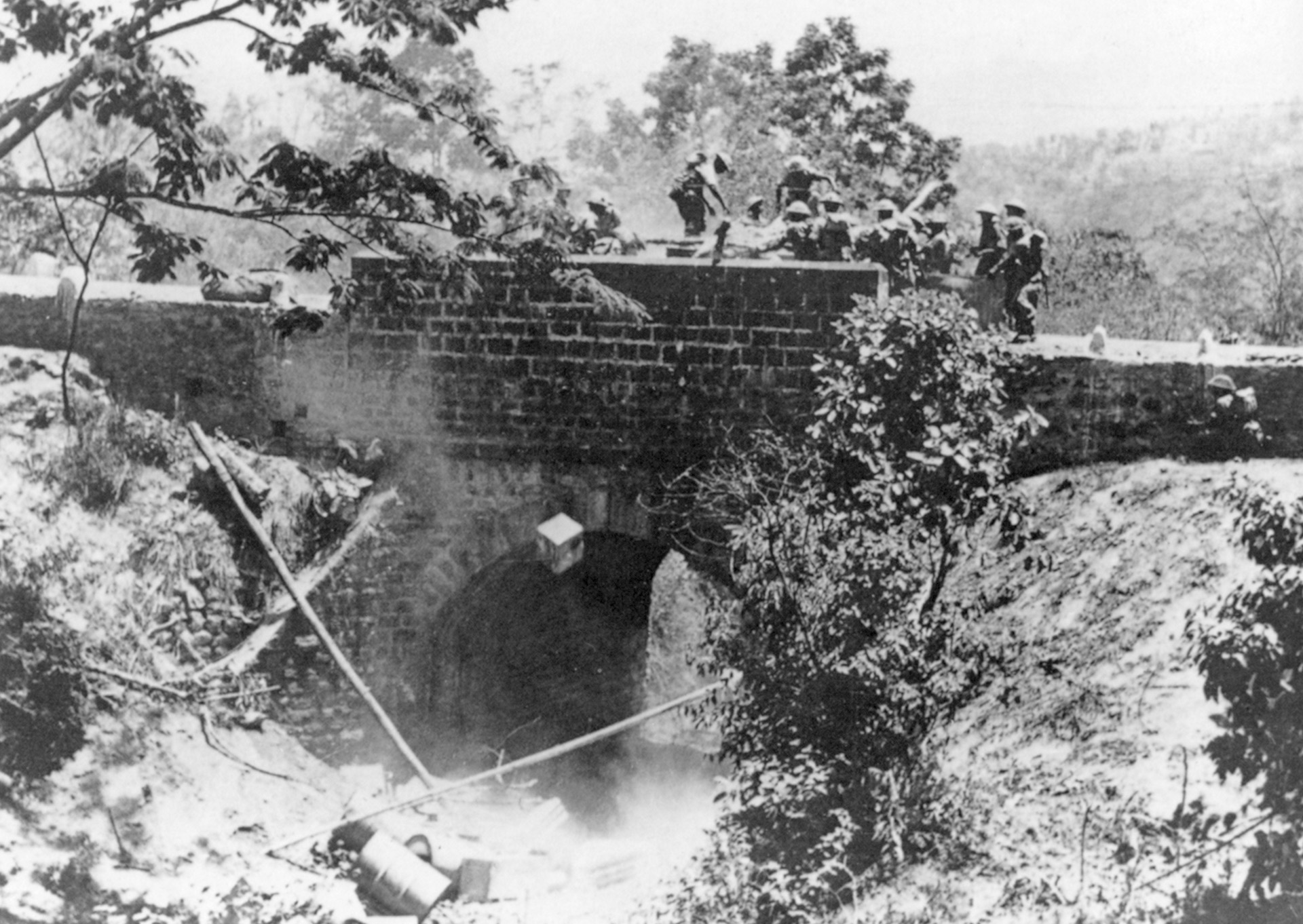 Sappers clear obstructions from a barricaded bridge. The Japanese moved through back country to descend on roads and set up their blockades.
