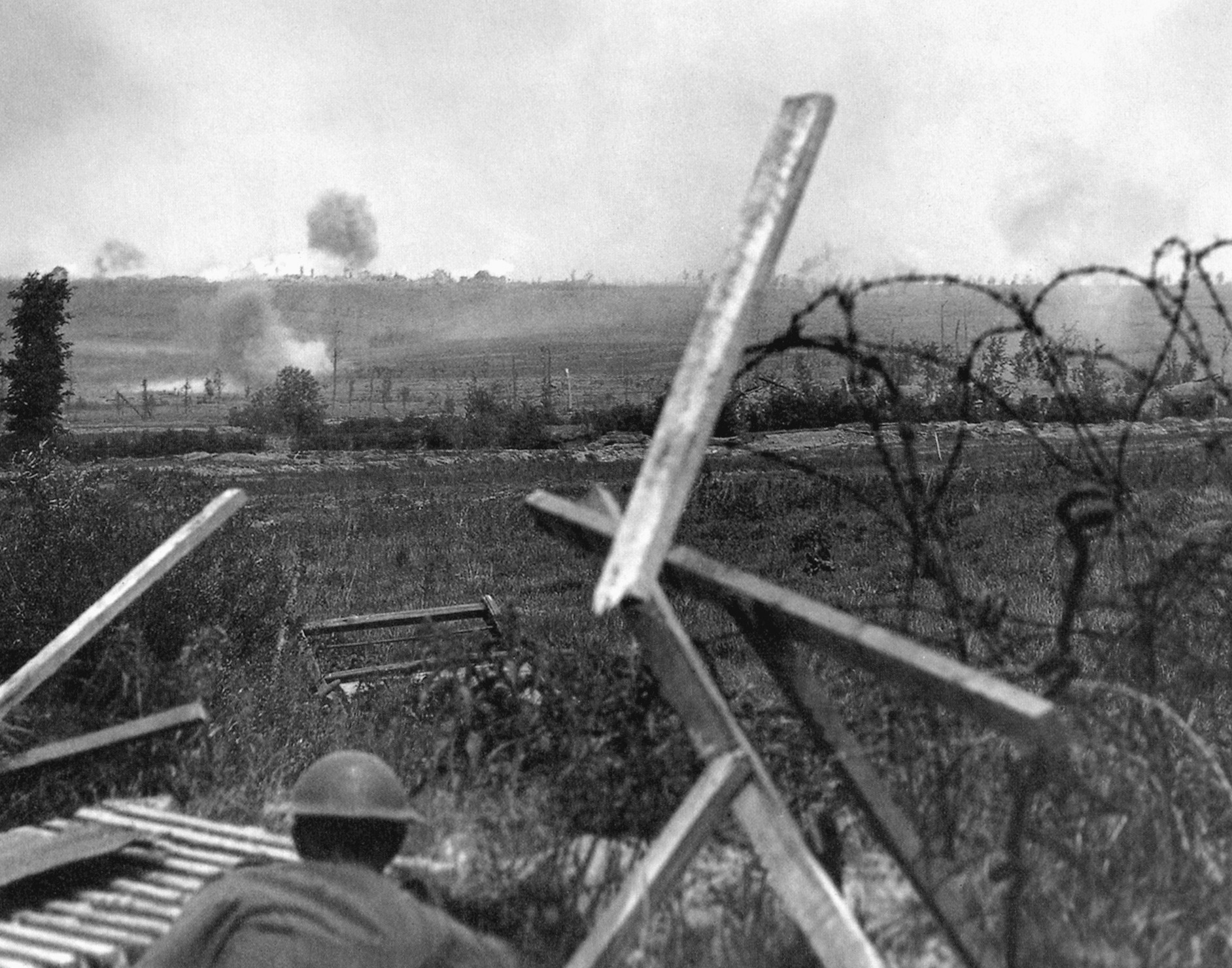 A British soldier crouches low as explosions light up a German-held ridge across the Douve valley.
