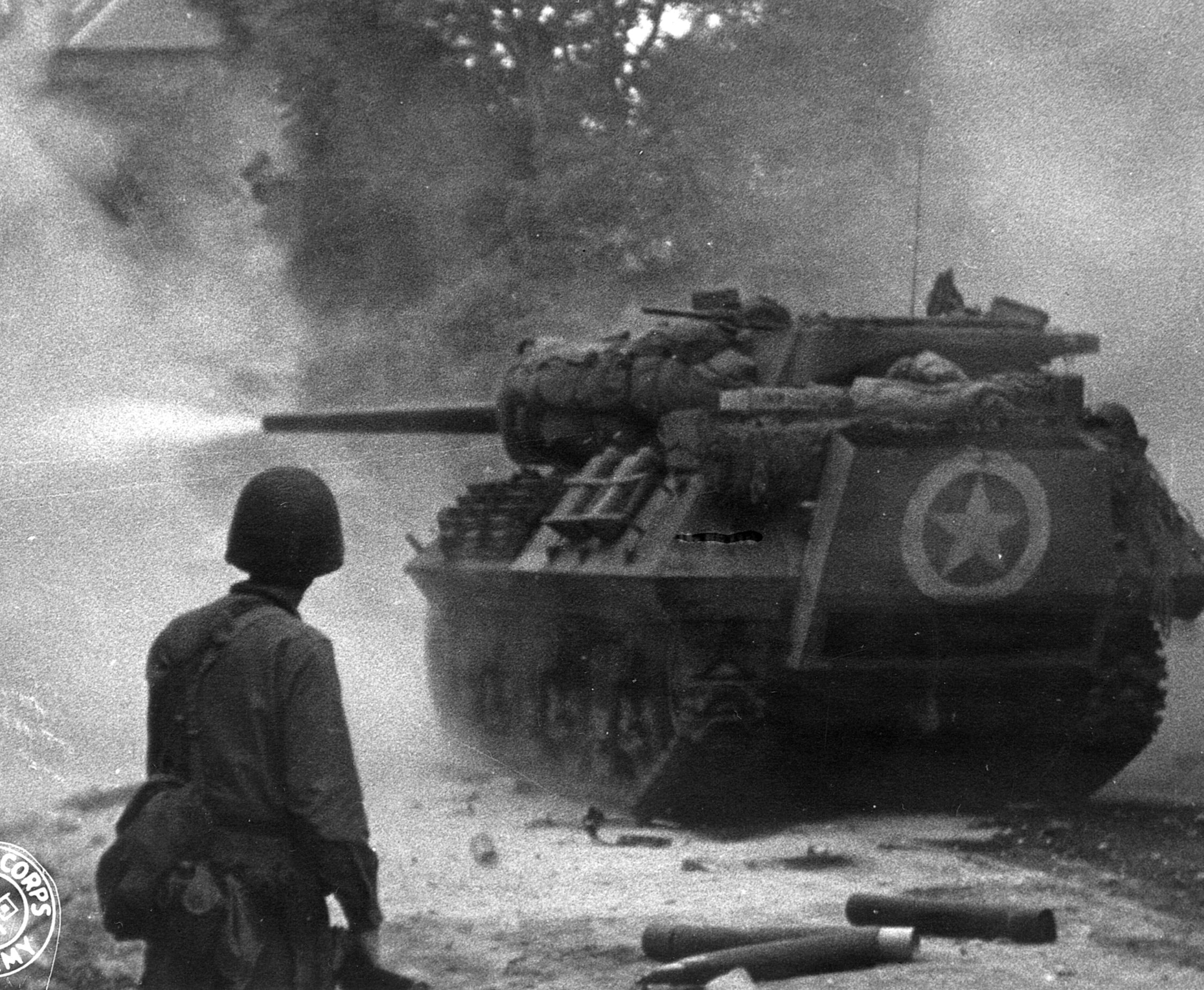 Firing away at retreating Germans in St. Lô, an American tank destroyer is watched attentively by a GI who is undoubtedly glad to have such firepower nearby.