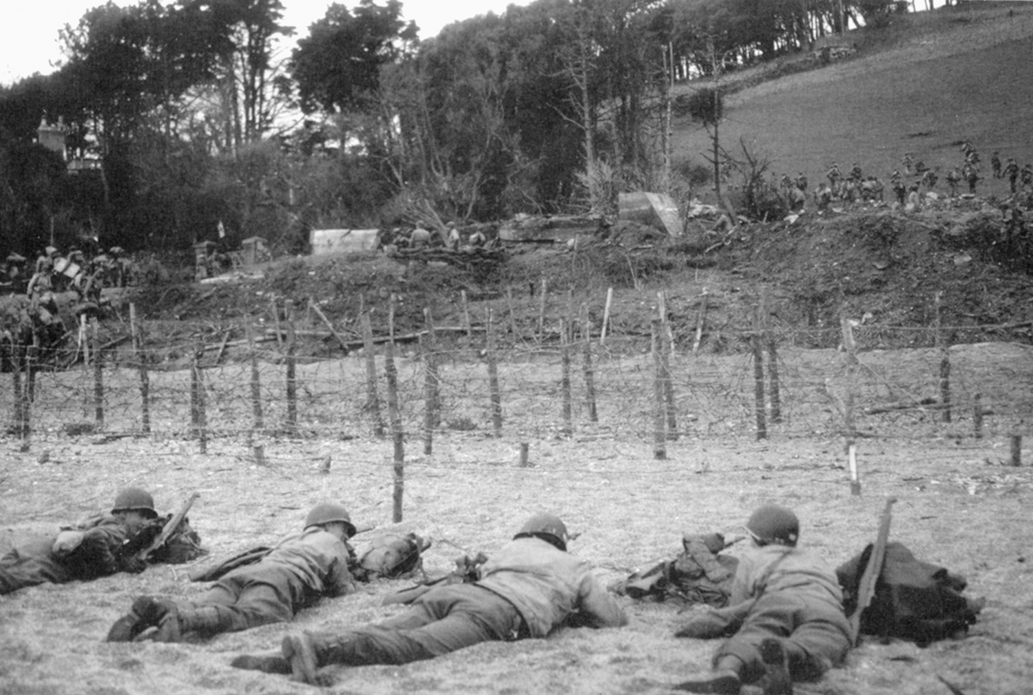 Lying low in front of beach obstructions during a live-fire exercise at Slapton Sands, U.S. soldiers await orders to advance. 