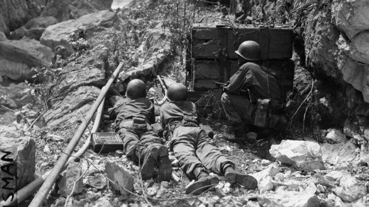 With a spillway for the Wawa Dam before them, three American infantrymen manning a .50-caliber machine gun provide cover for an advance patrol.