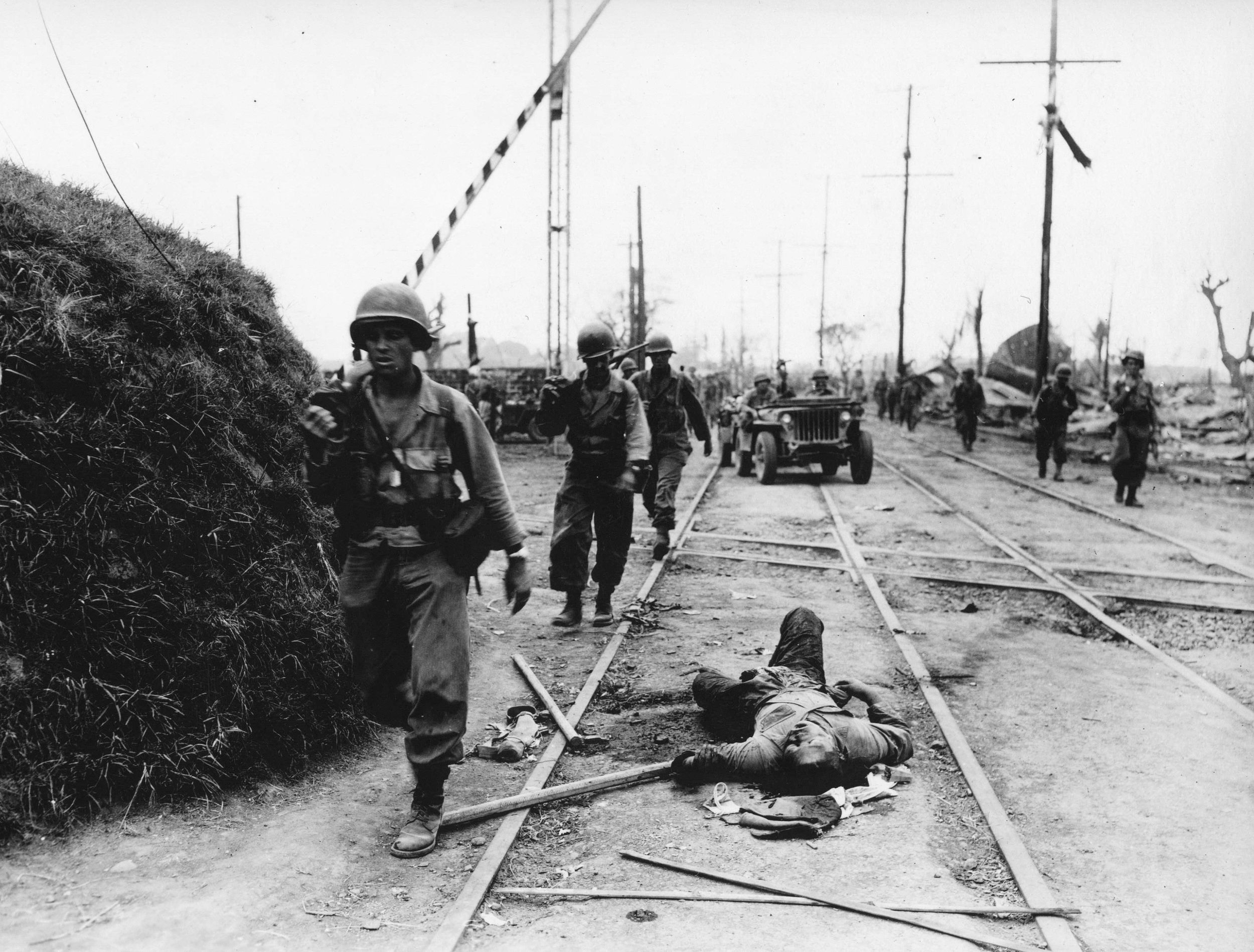 Some fanatical defenders decided to fight to the death in Manila. American soldiers of the 1st Cavalry Division trudge past the bodies of several of the Japanese dead.