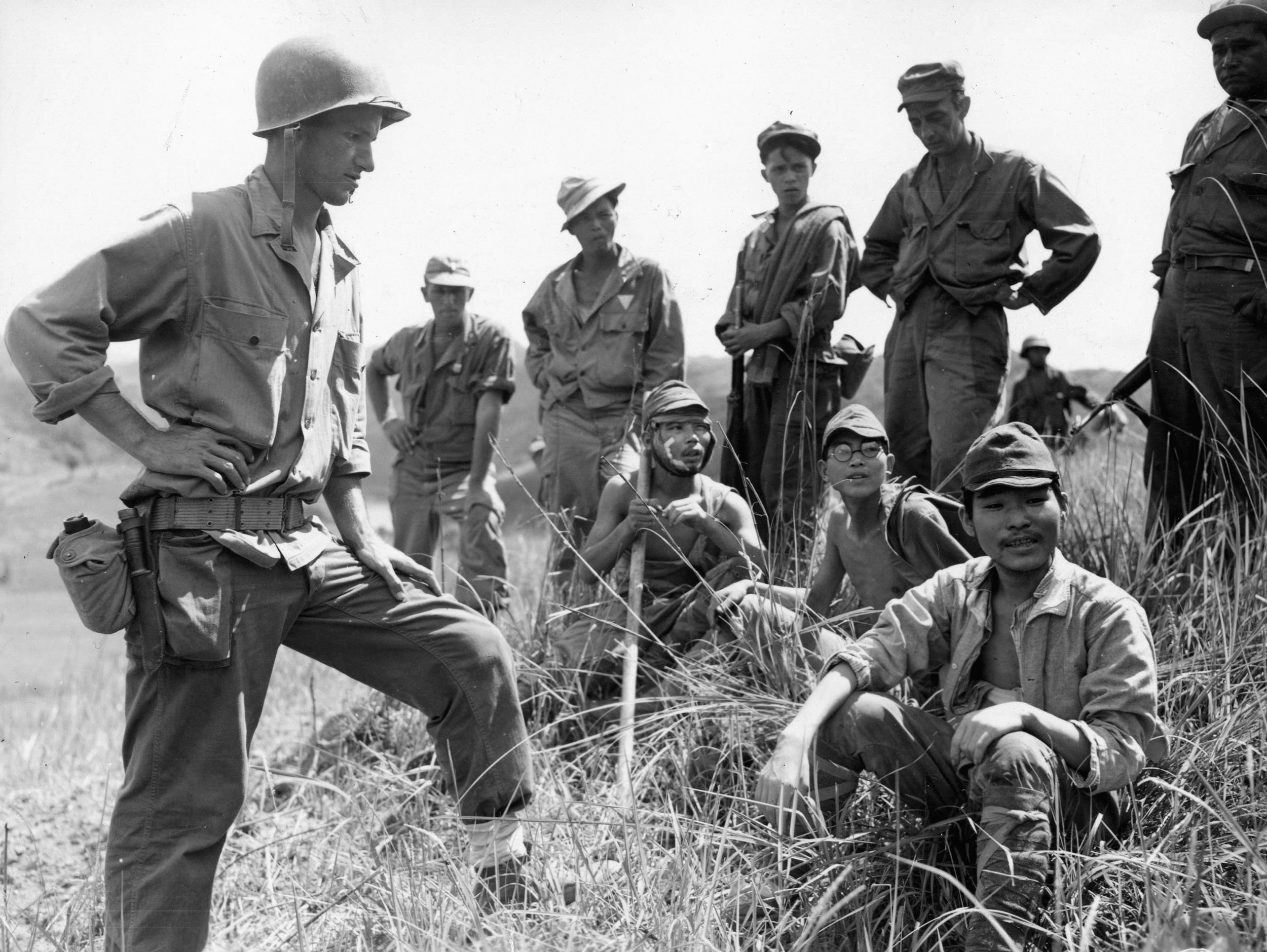A rare sight, three Japanese prisoners captured during the fighting around the Ipo Dam sit on the ground surrounded by their American captors. 