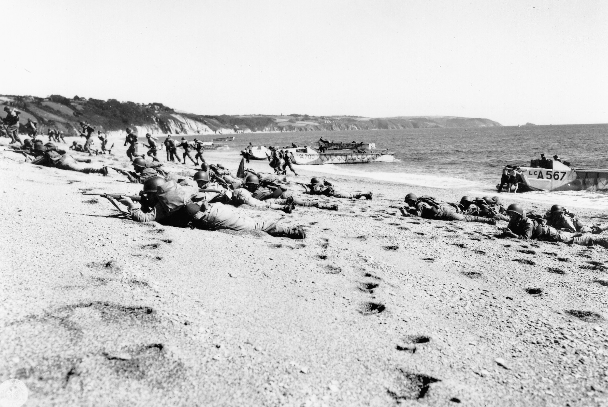 On a beach in England, British and American troops perform preparatory battle exercises.