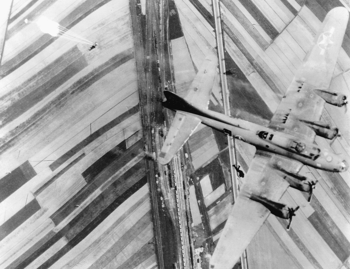Two members of a B-17 bomber crew bail out of their stricken craft over a patchwork countryside in Germany.  